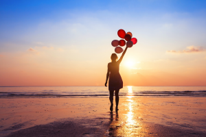 Calming beachscape with woman holding balloons and letting go